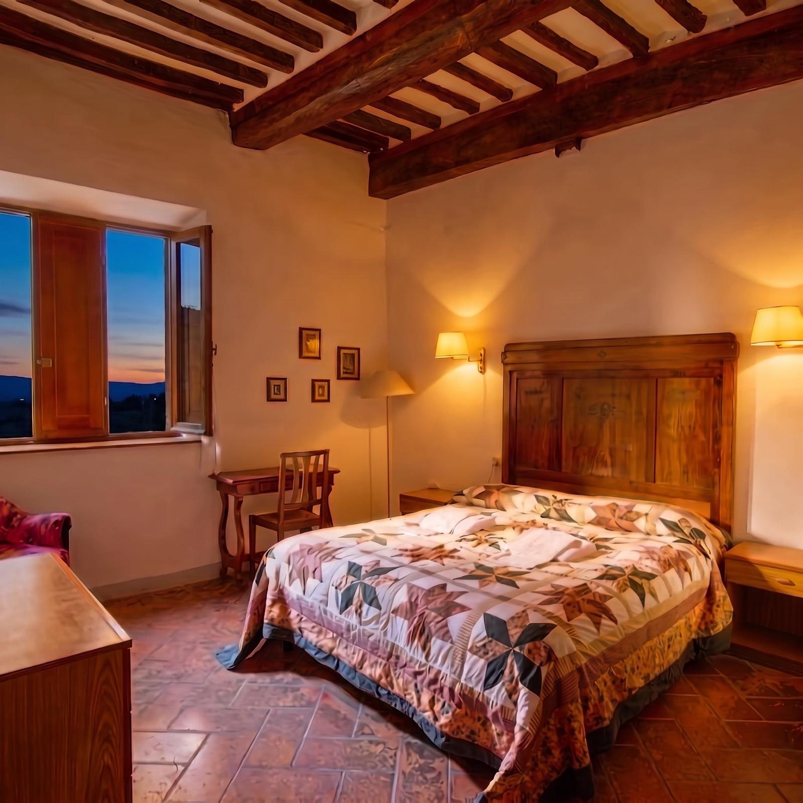 Camera matrimoniale con testata in legno e finestra sulle colline al tramonto